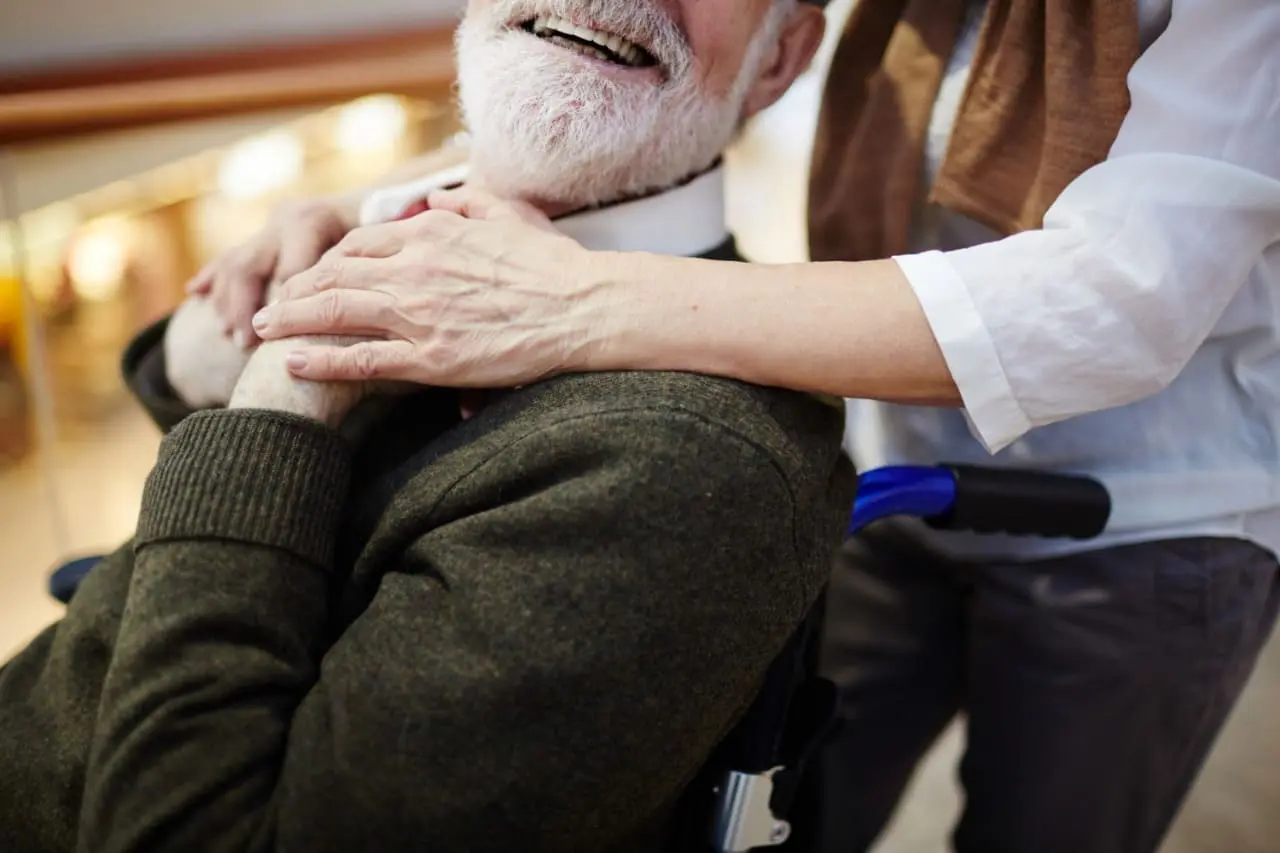 Carer in white uniform holding hands of elderly man in wheelchair, providing compassionate personal aged care support services with Acals Australia