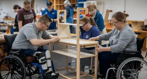 Two NDIS participants in wheelchairs building a wooden frame in a workshop, supported by an instructor at Acals upcycle and recycle woodworking program Sydney