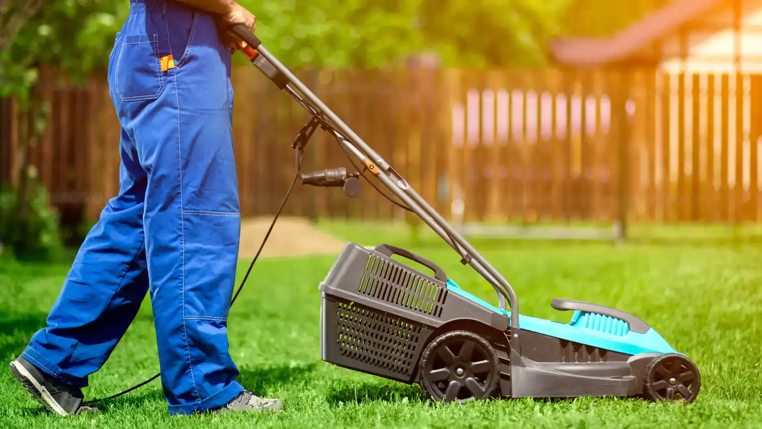 Worker in blue overalls mowing lawn with electric lawnmower for Acals home gardening support services for aged care and NDIS participants